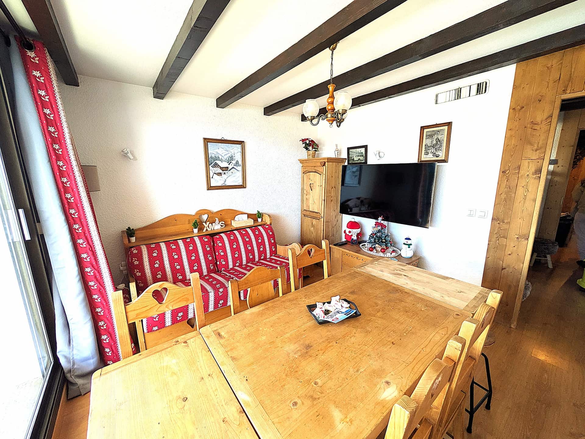 Séjour de l'appartement La Lauzière avec table en bois massif, canapé savoyard et poutres apparentes